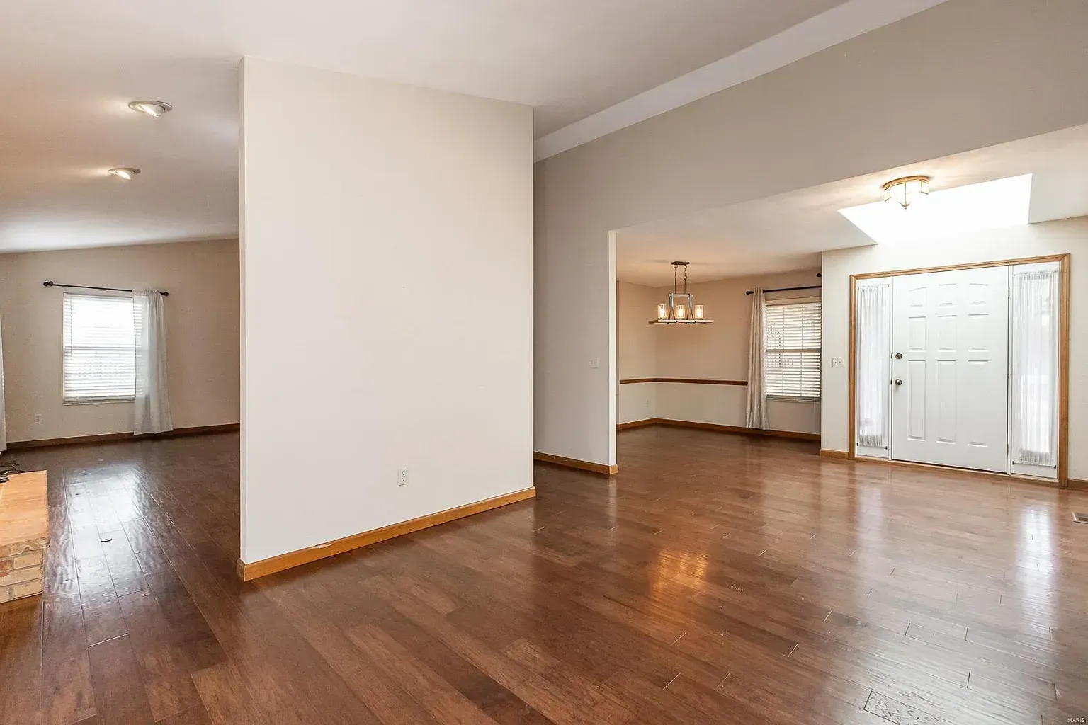 Empty living room with wood floors, neutral walls, and natural light.