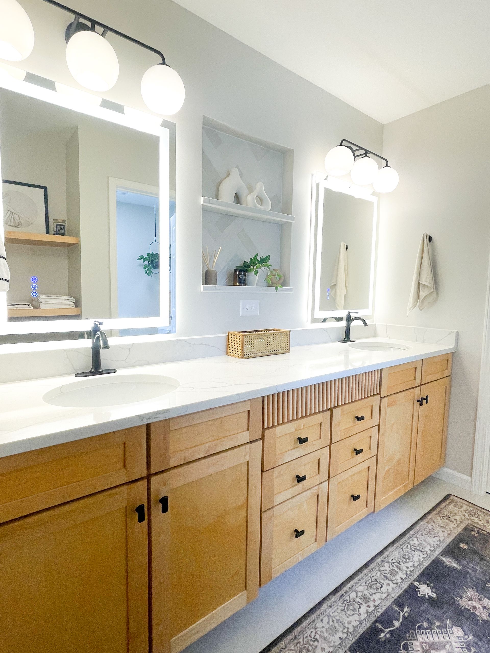 Modern bathroom with floating wooden vanity, white countertops, two sinks, and illuminated mirrors.