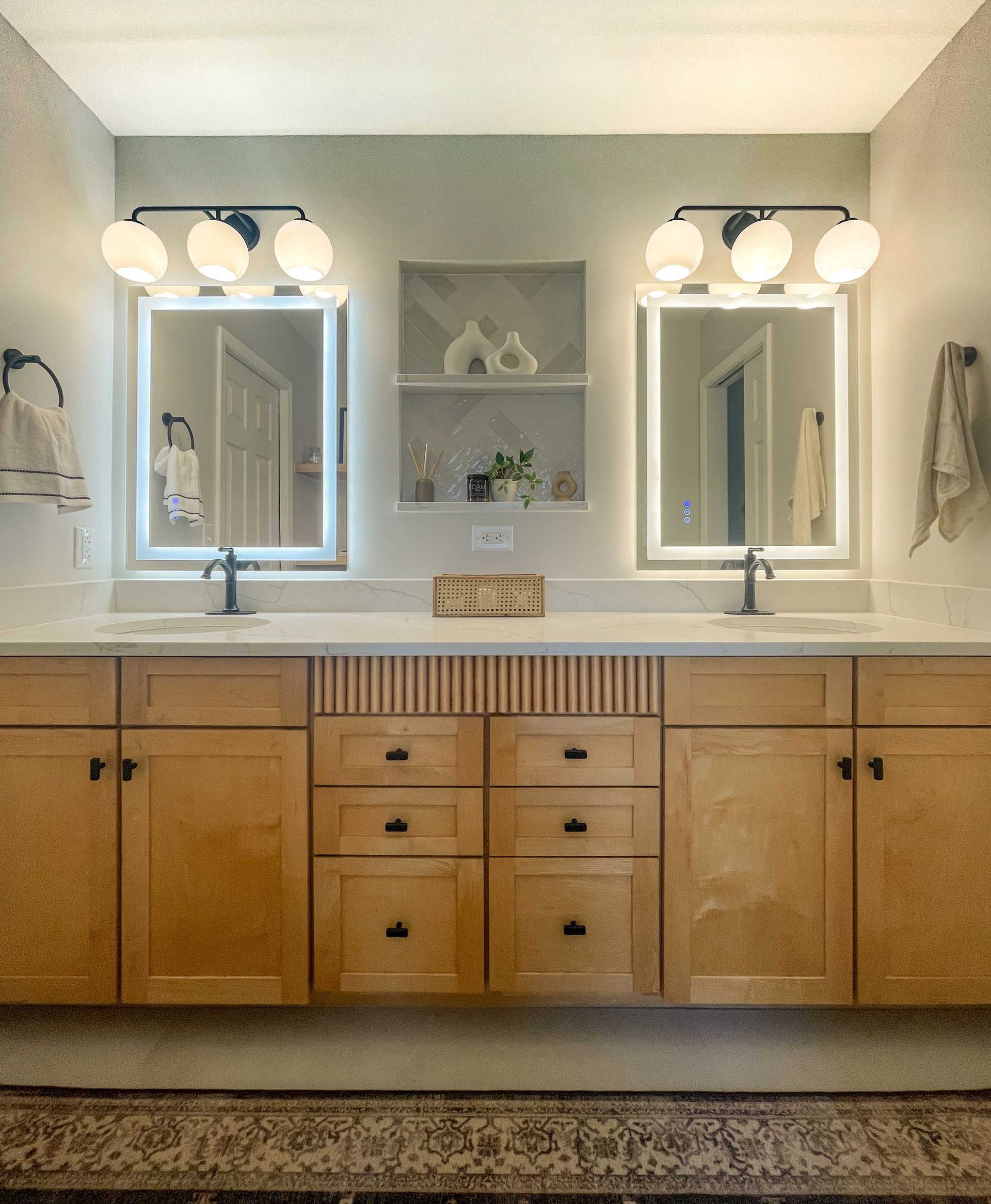 Bathroom with dual sinks, wooden vanity, and modern light fixtures over two mirrors.