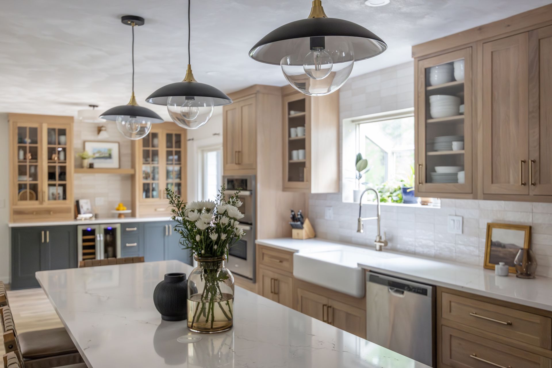 Modern kitchen with light wood cabinets, white countertops, and black pendant lights.