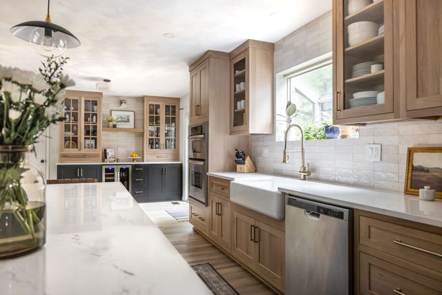 Modern kitchen with light wood cabinets, white countertops, and black pendant lights.