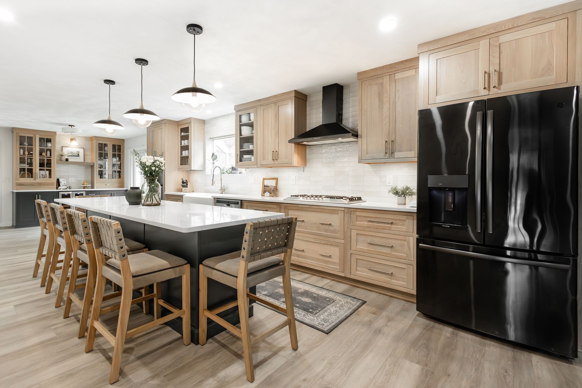 Modern kitchen with a black island, light wood cabinets, and white countertops, o'fallon, IL remodel, renovation, white oak cabinets, custom kitchen, stacked horizontal cloe backsplash tile, nathan james barstools, top knobs hardware, sherwin williams iron ore paint color, bright and refreshing kitchen