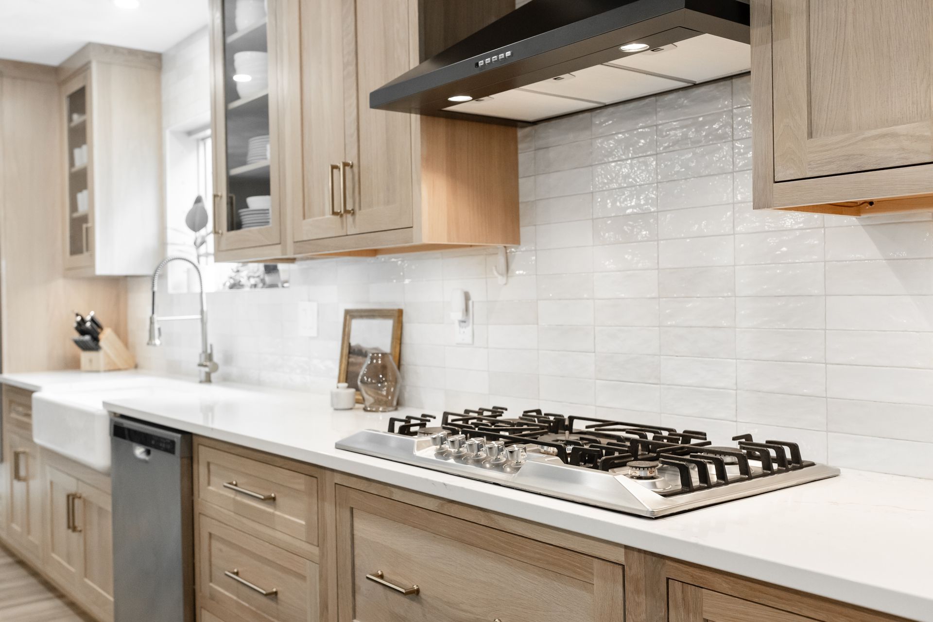 Modern kitchen with light wood cabinets, white countertops, and stainless steel gas stove.