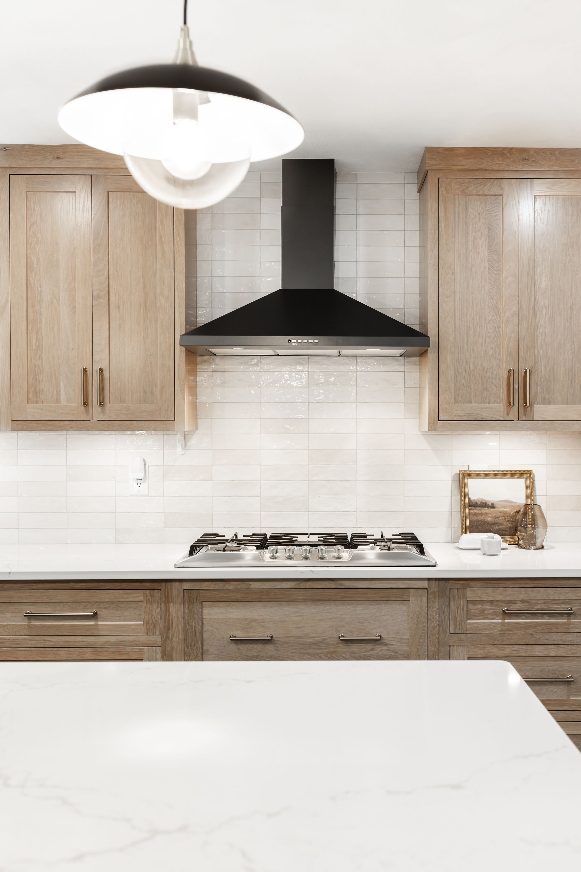 Kitchen with wood cabinets, white countertops, black range hood, and pendant light.