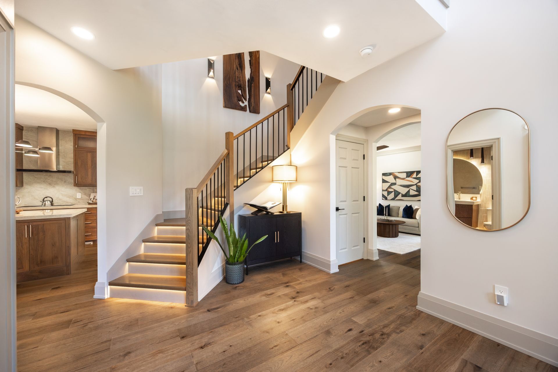 Custom staircase with LED lighting, light wood steps, black wrought iron railing, white or light gray walls, contrasting trim, leading to a lower level, custom wood wall art, modern wall sconces, modern transitional design, remodel in Edwardsville, IL