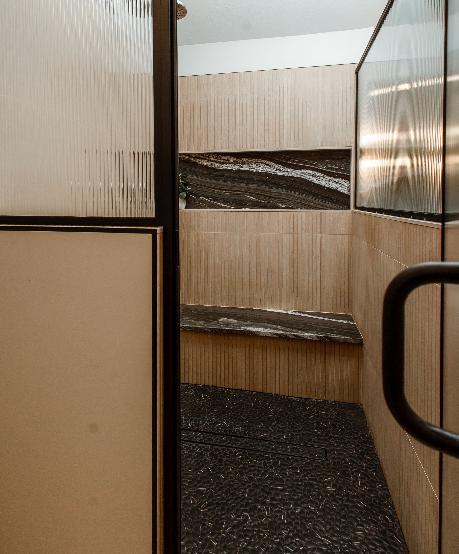 Shower stall with pebbled floor, built-in bench, and textured glass door and walls.