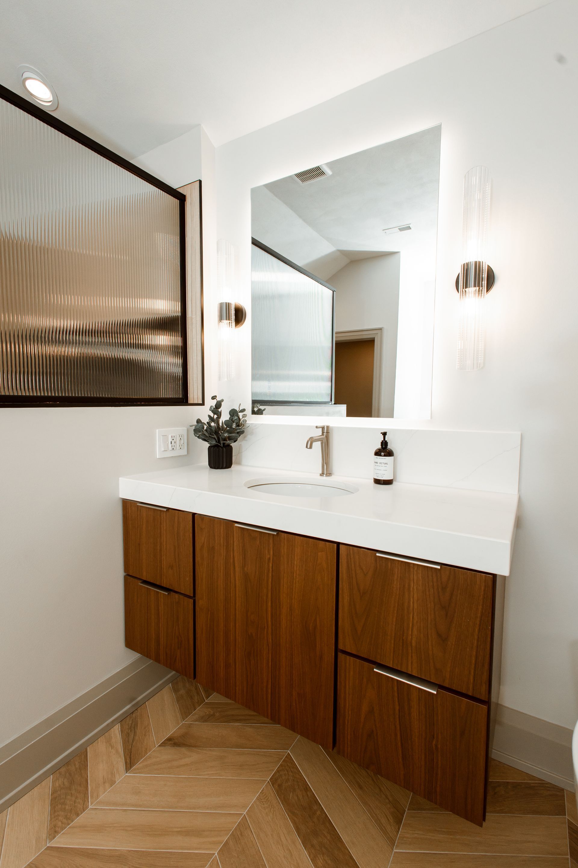 Modern bathroom vanity with wood cabinets, white countertop, large mirror, and sconces.