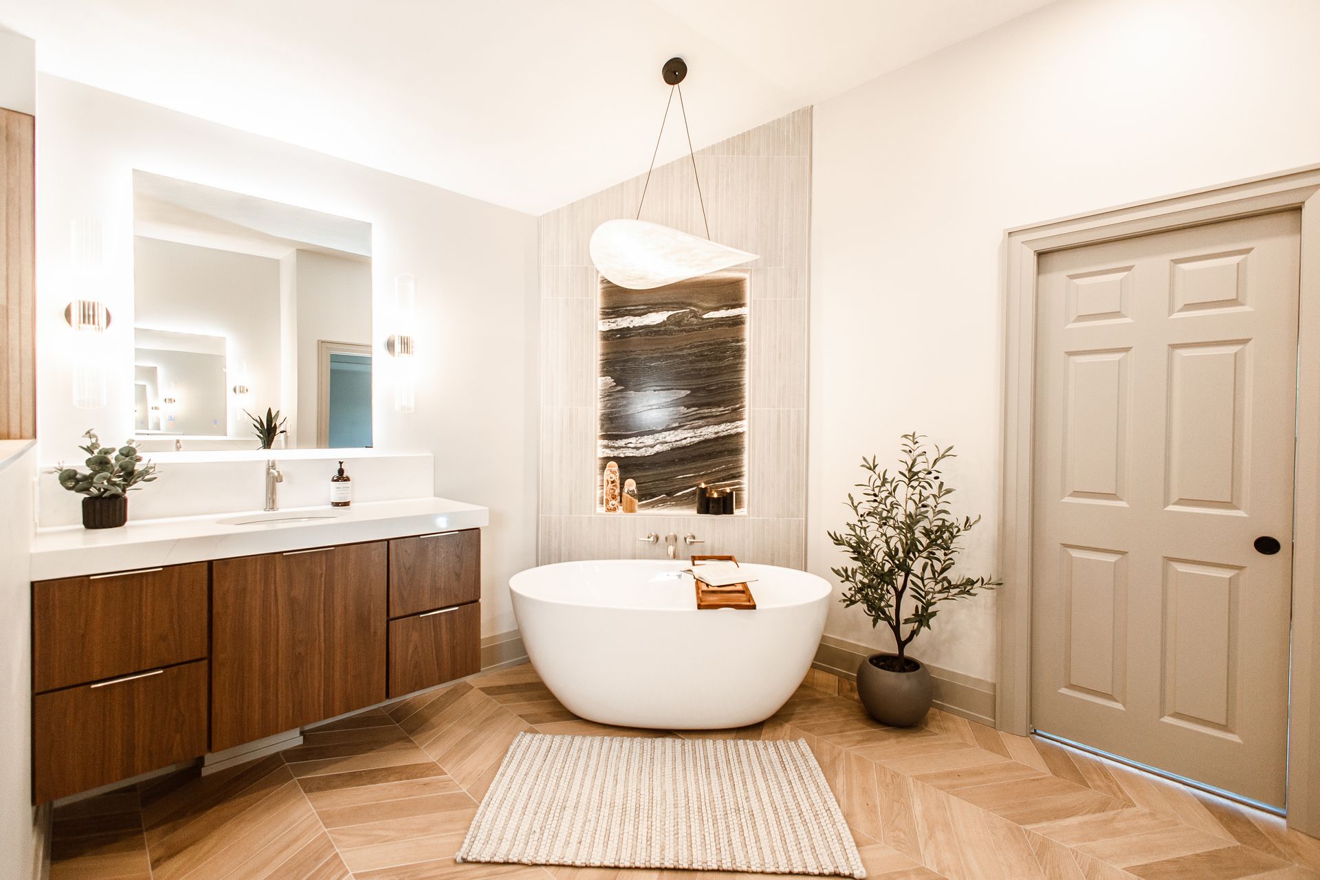Modern bathroom with a white freestanding tub, wooden vanity, and herringbone floor.