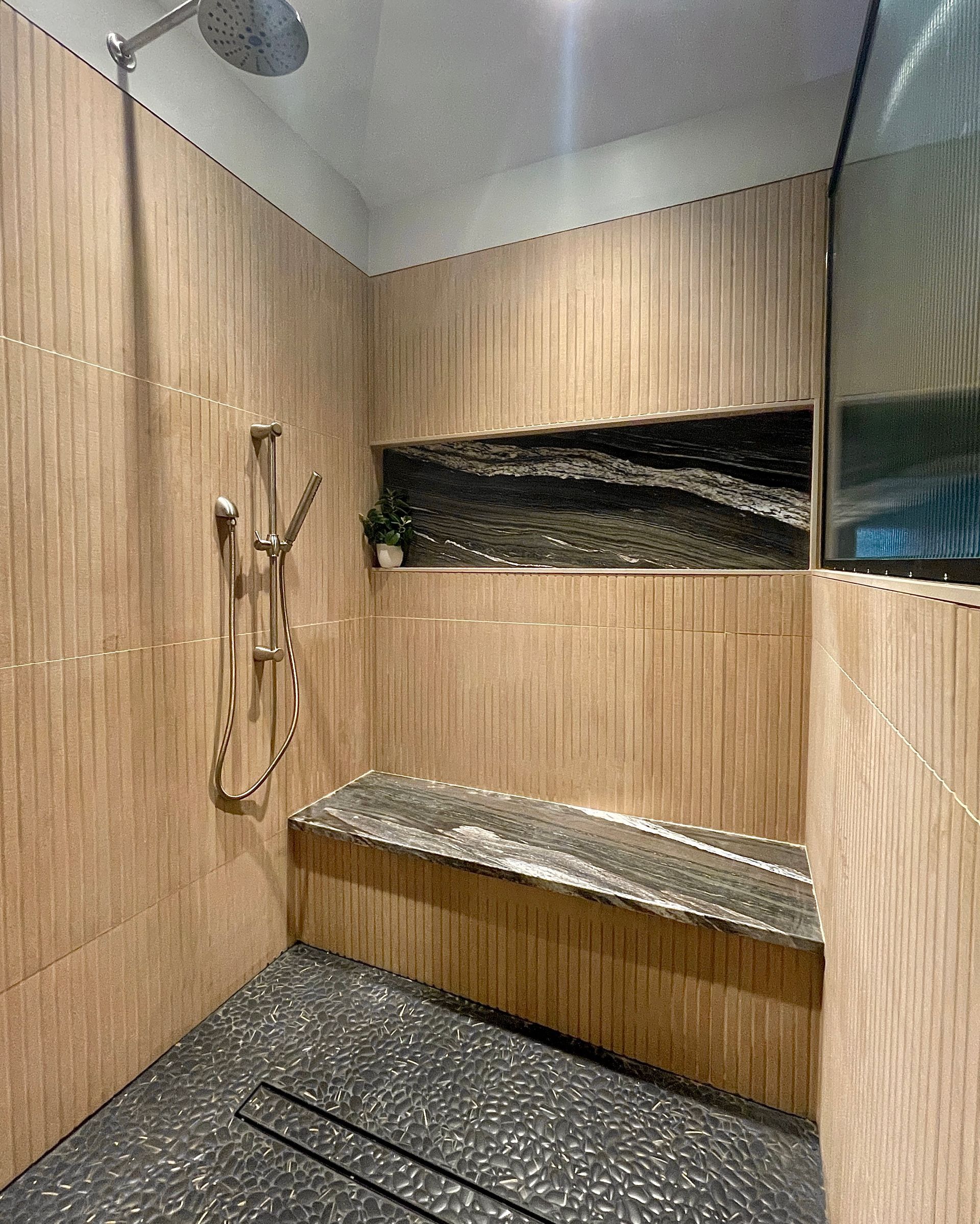 Shower with light wood-look tiled walls, dark stone bench, and built-in niche.