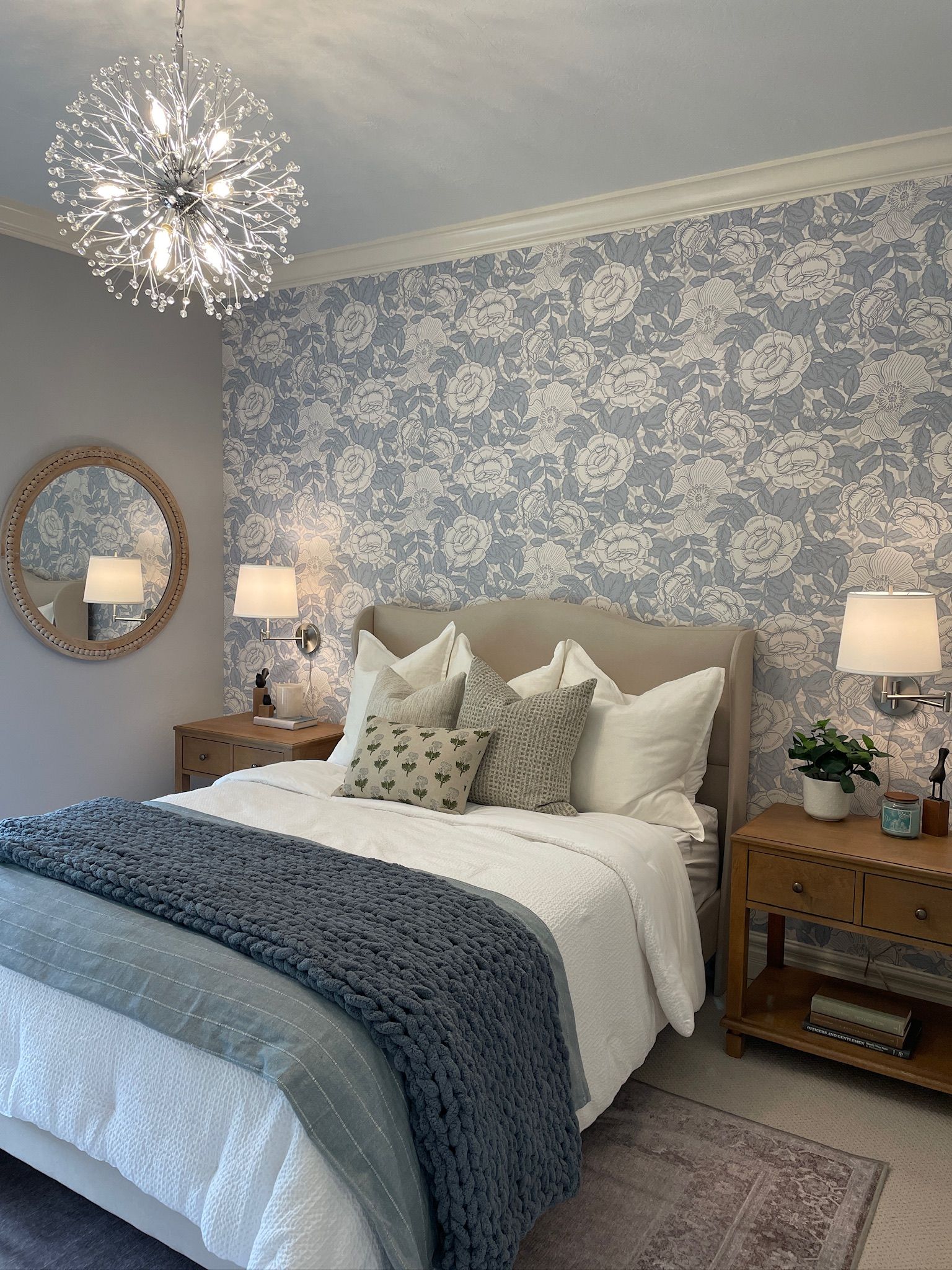 Bedroom with blue and white floral wallpaper, wooden bedside tables, and a bed with white and blue bedding.