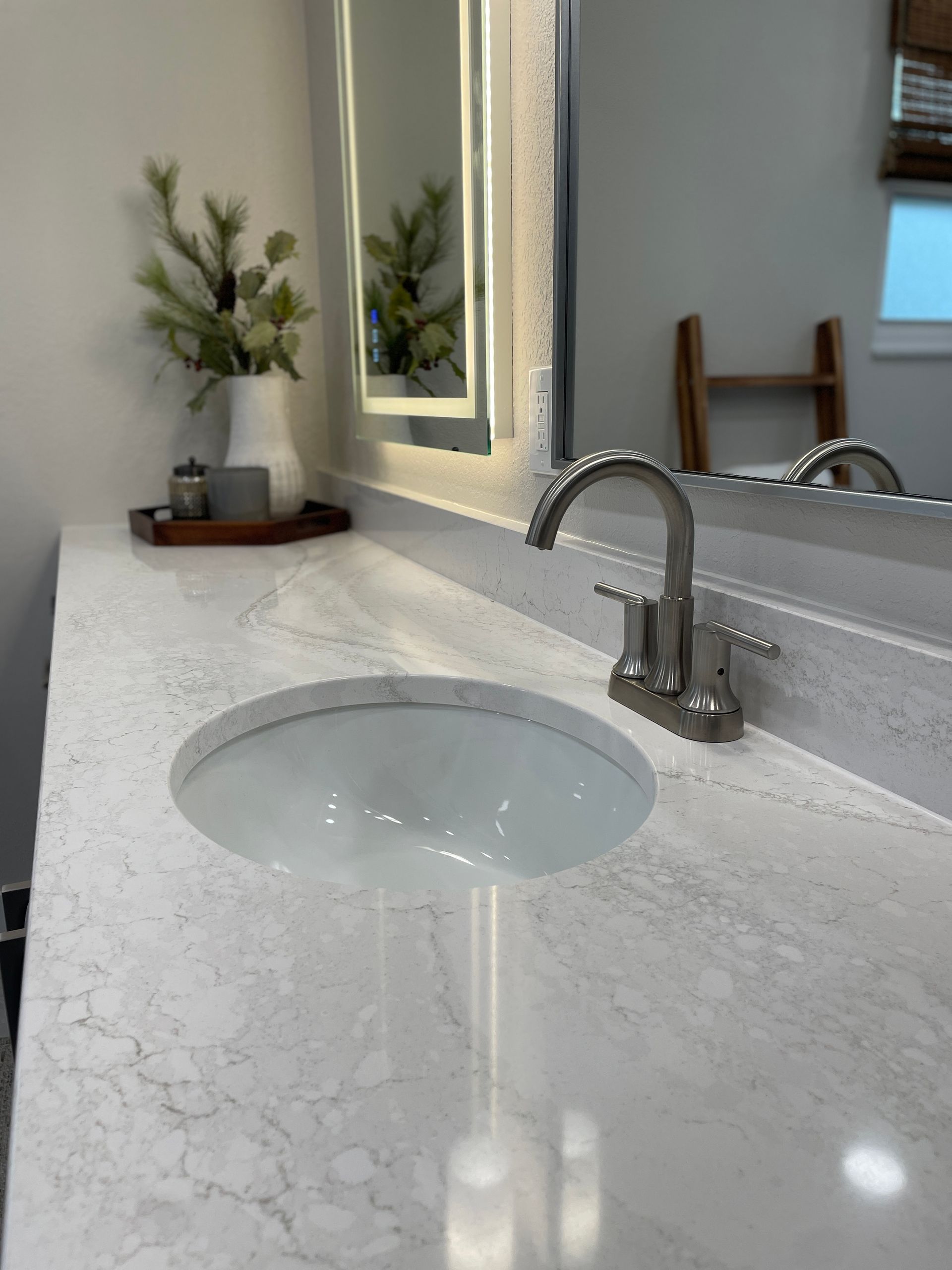 Bathroom vanity with a round sink and faucet. A mirror reflects a wooden ladder and vase of greenery.