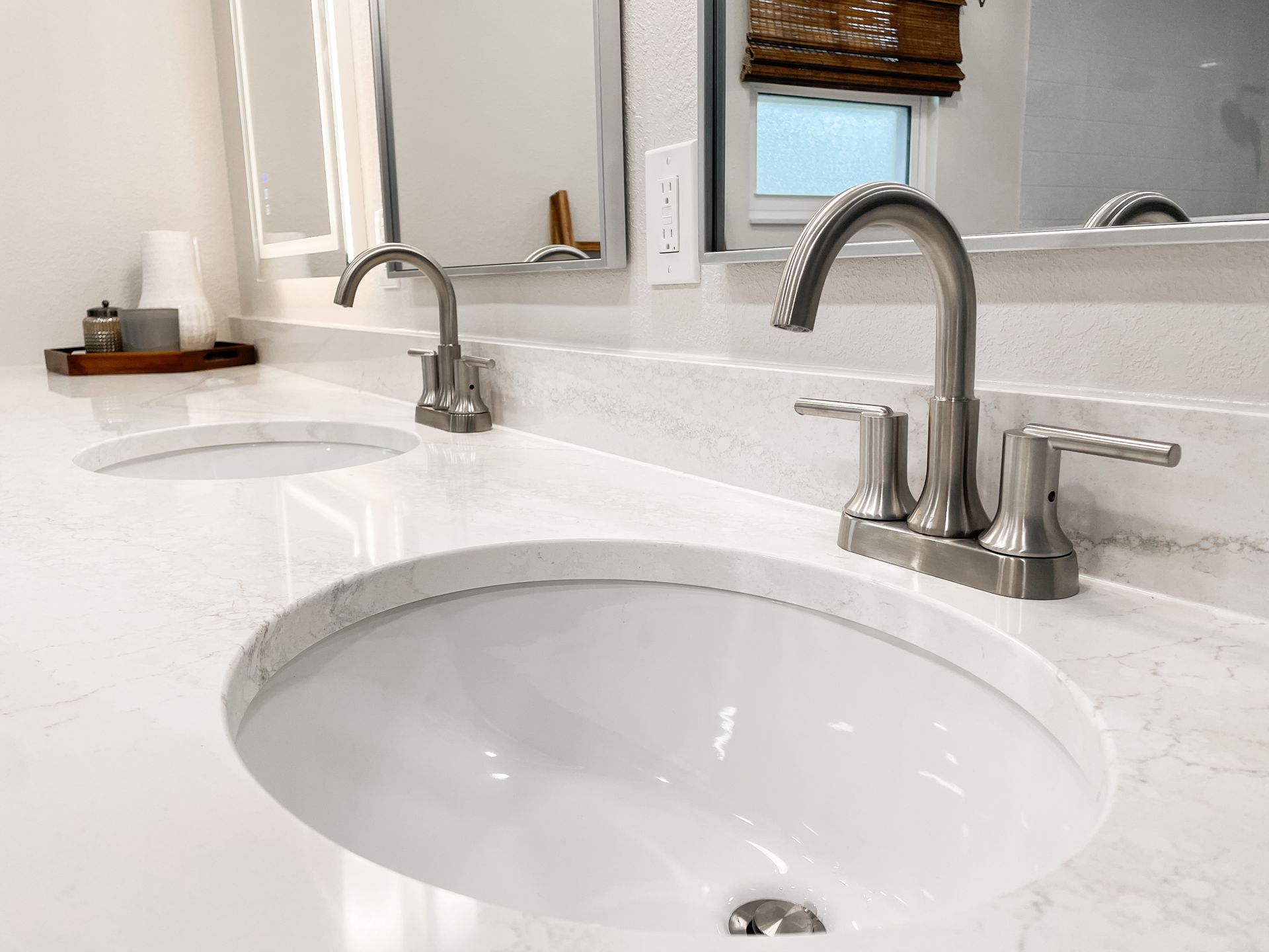 Bathroom with two white sinks, chrome faucets, and a light-colored countertop. Mirrors and a window are visible.