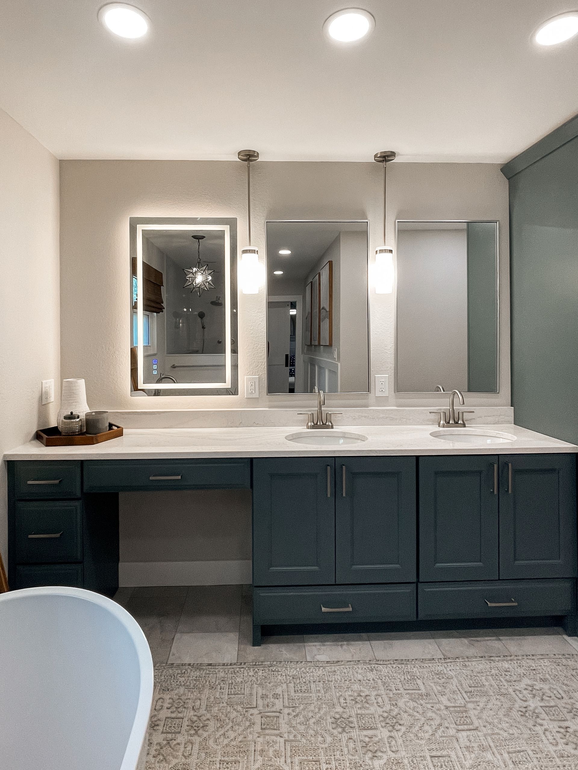 Bathroom with blue cabinets, three mirrors, and white countertop. A lit mirror is on the left.