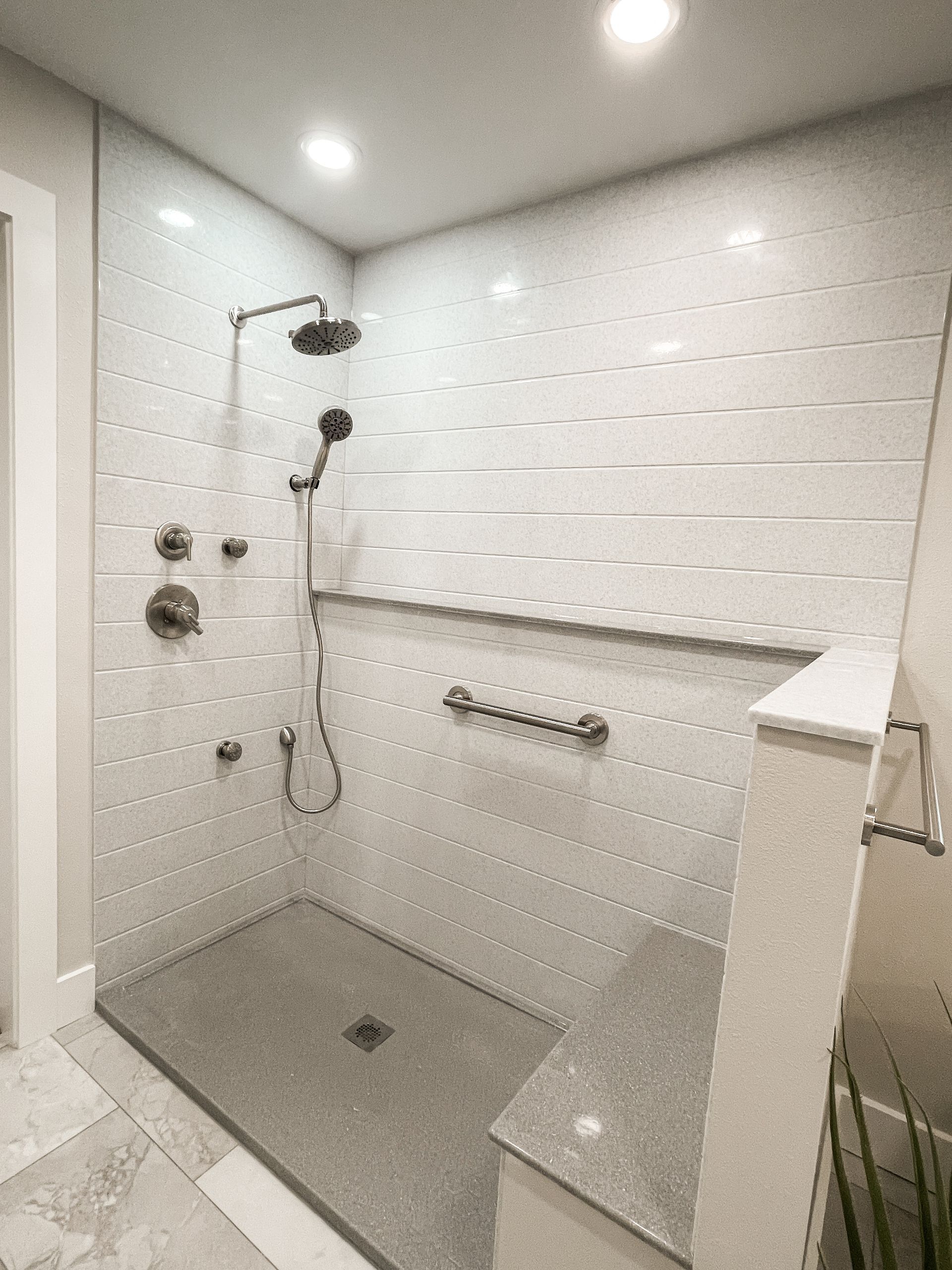 Accessible shower with gray tile, bench, and grab bar.