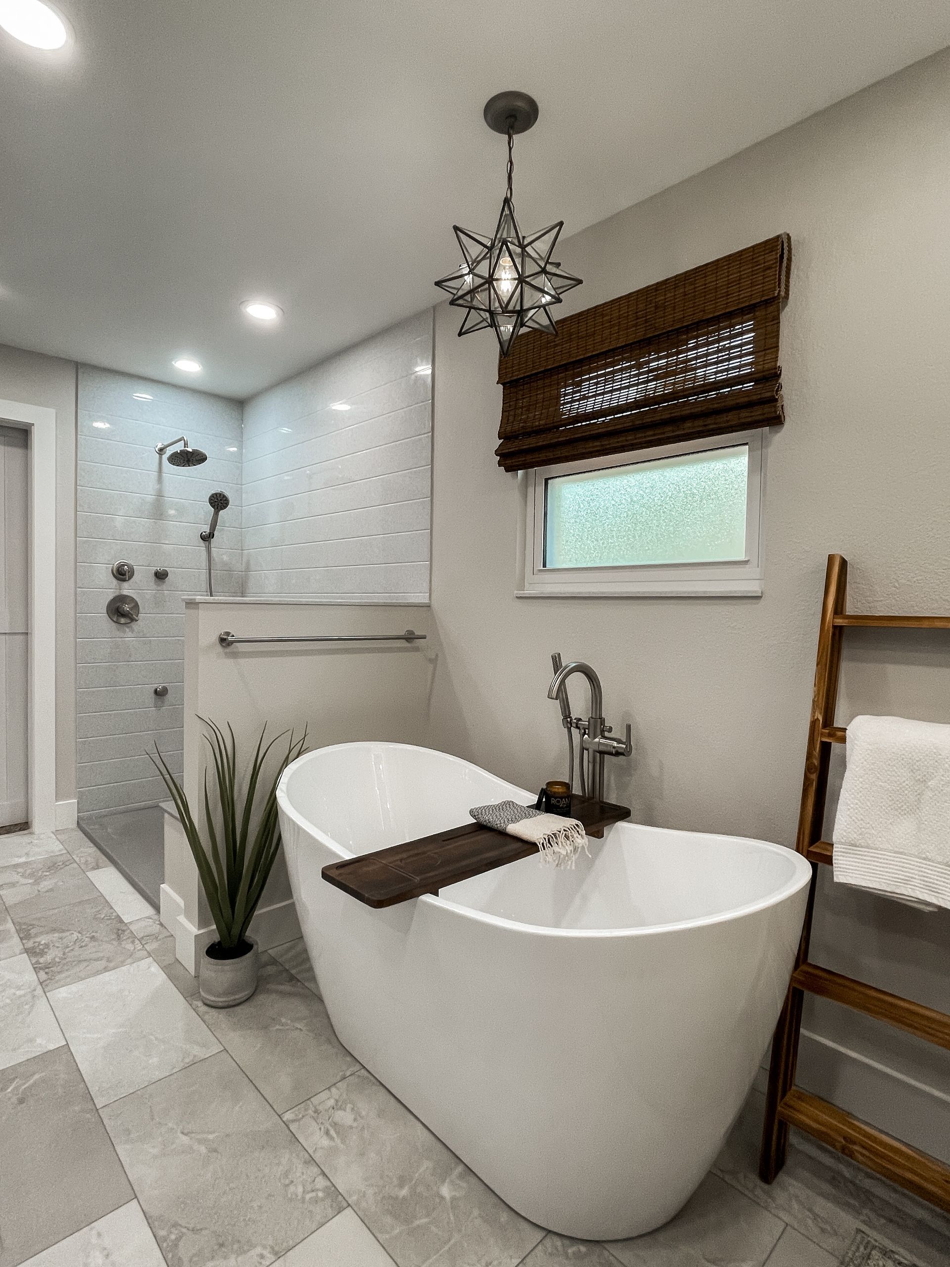 Modern bathroom with a white freestanding tub, shower, and a wooden ladder.