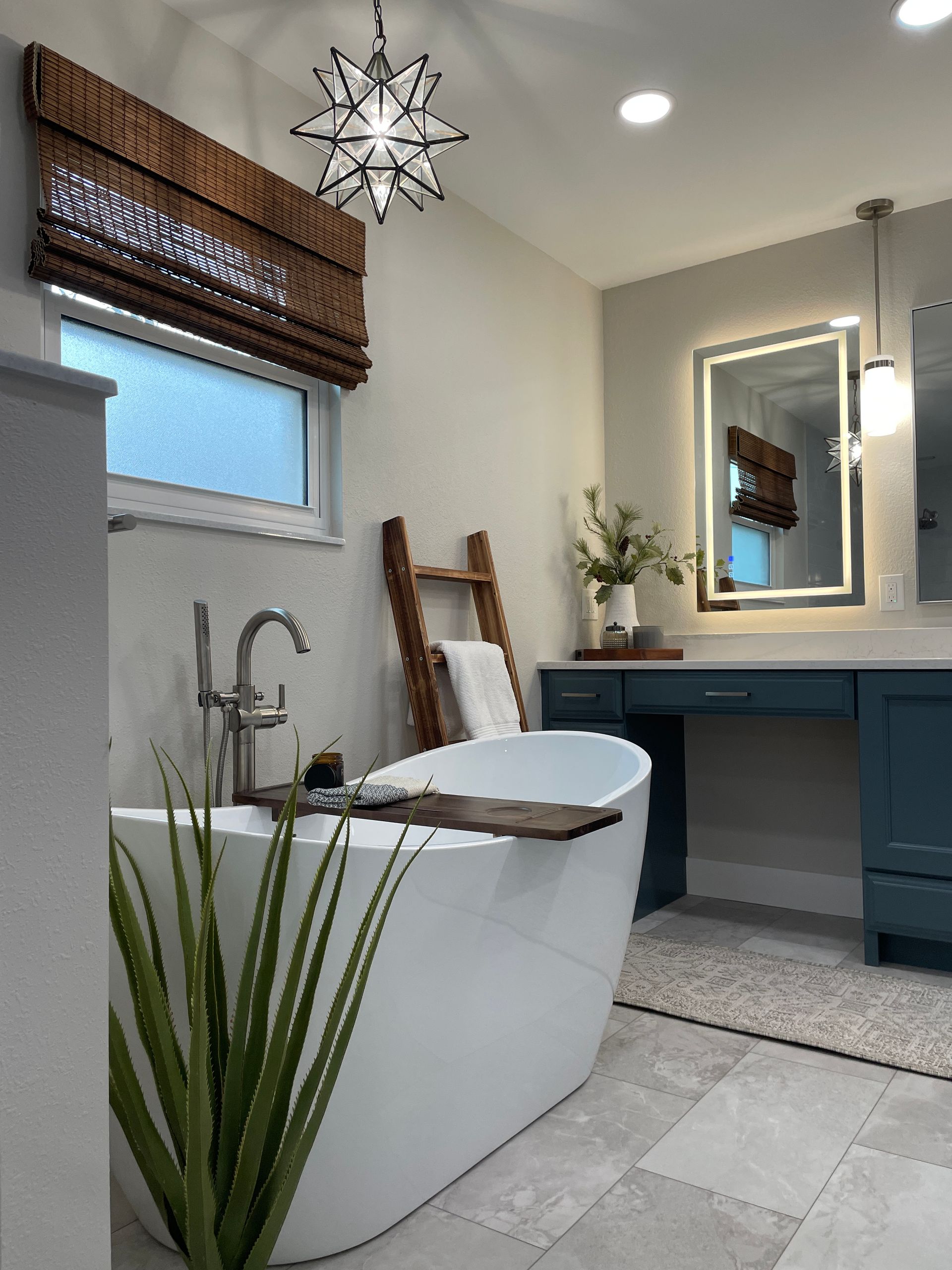 Modern bathroom with white tub, blue vanity, woven shade, starburst light, and gray floor tiles.