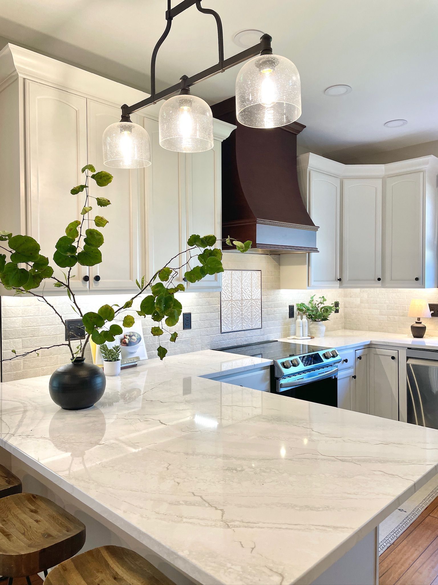 Bright kitchen with white cabinets, marble countertop, and pendant lights. A vase of greenery sits on the counter.