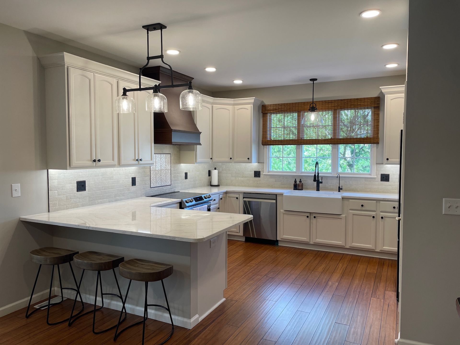Modern kitchen with white cabinets, stainless steel appliances, and wood flooring. Features a breakfast bar and window.