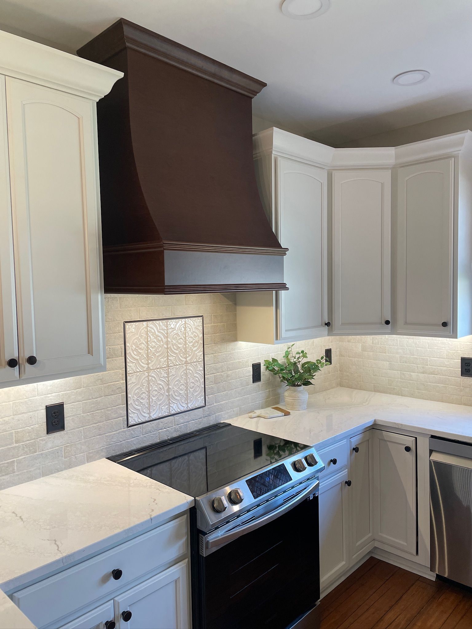 A kitchen with white cabinets, a dark brown range hood, and a black stovetop.