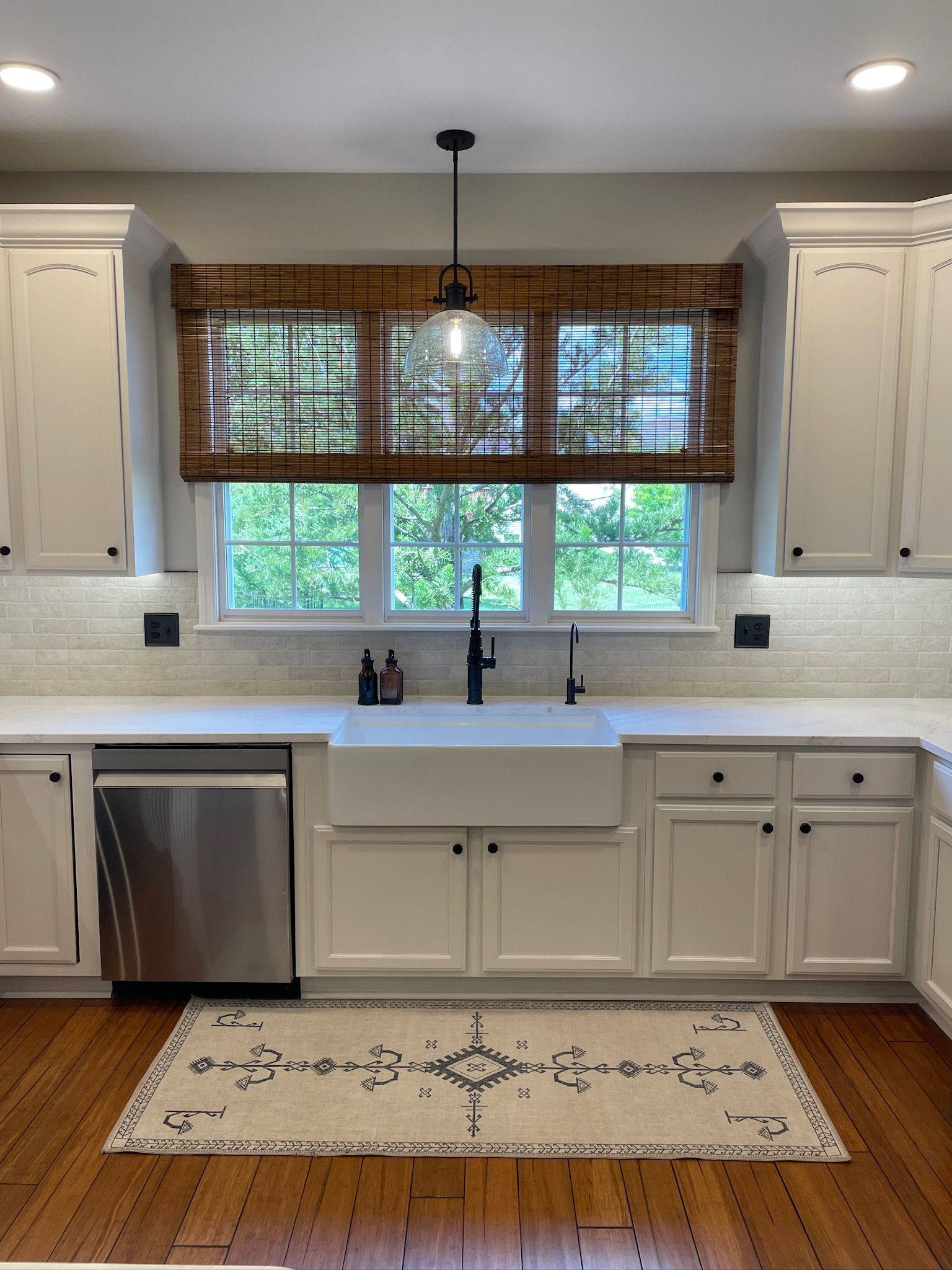 White kitchen with a farmhouse sink, under-cabinet lighting, and a window with a woven shade.