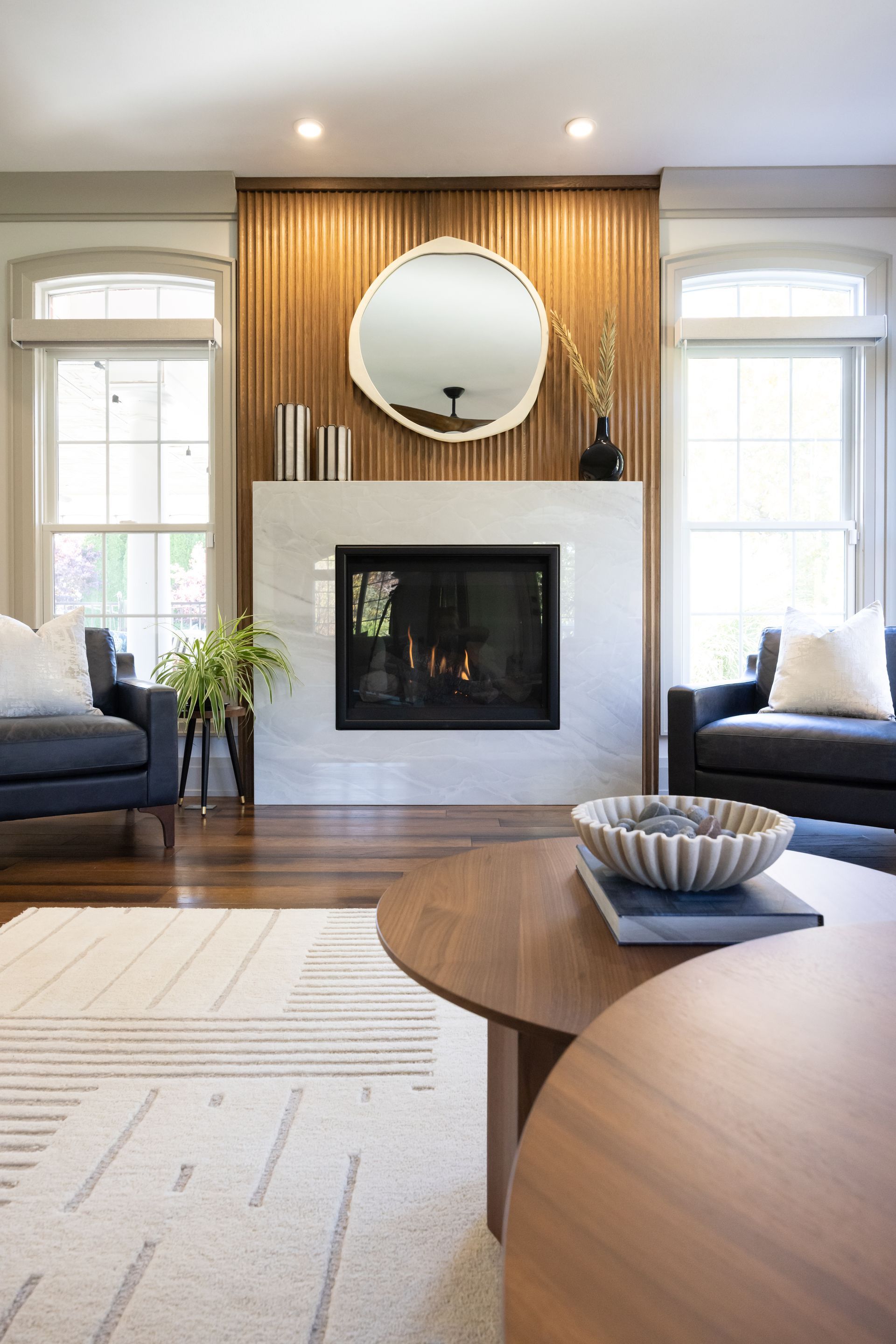 fluted wood wall, wood slat wall, porcelain stone fireaplace, mid century modern, transitional design style, modern living room, gas fireplace, engineered hardwood floor, remodel in Edwardsville, IL, navy lesther chairs, cozy living room, sherwin williams paint, soft gray walls, contrasting trim