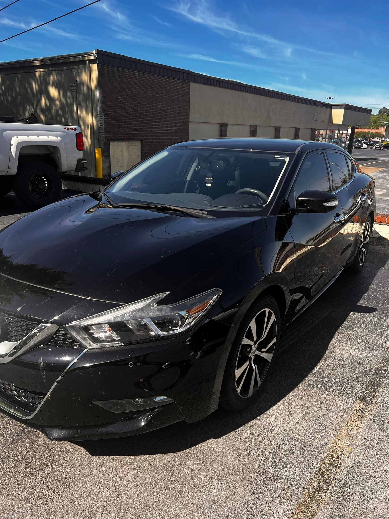 A black car is parked on the side of the road in front of a building.