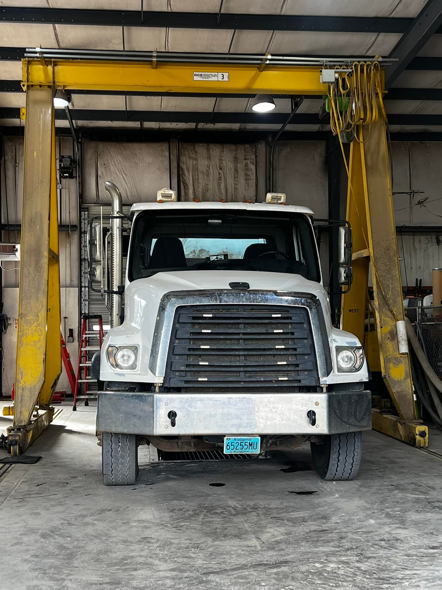 A white truck is parked under a yellow crane in a garage.