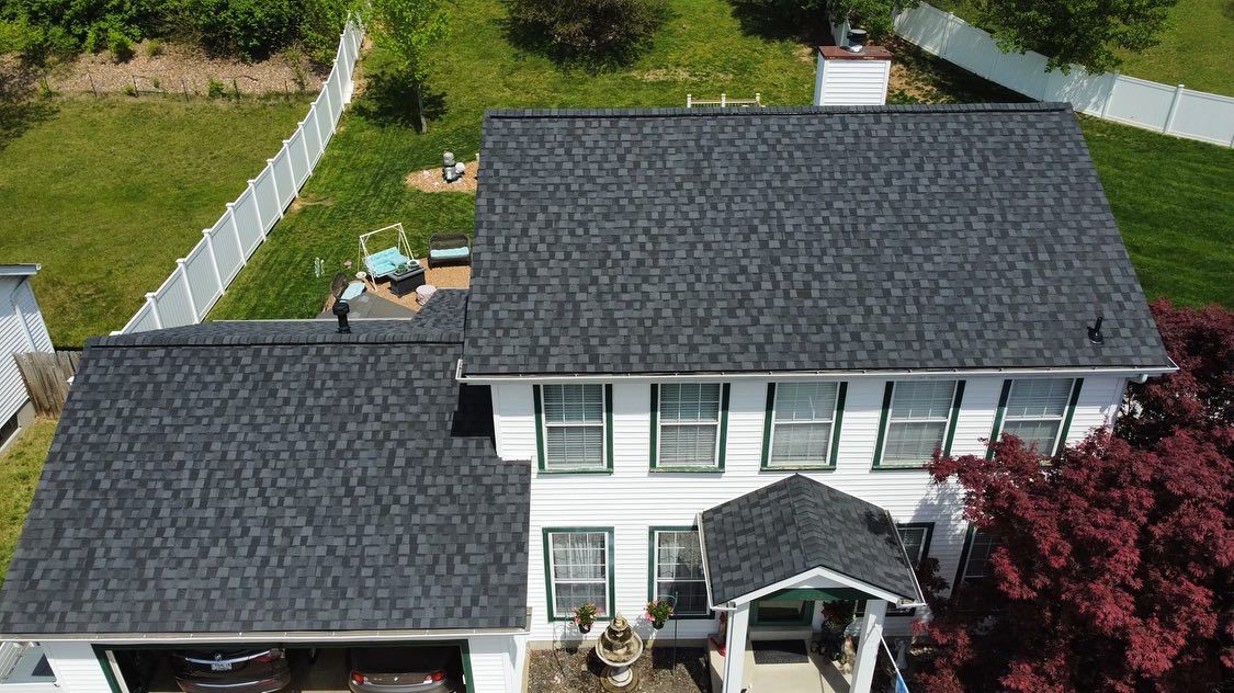 Aerial view of a white house with a dark gray shingled roof, set on green grass with a white fence.