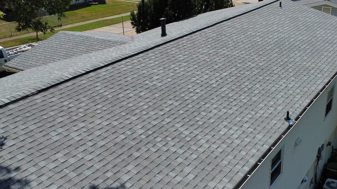 Gray asphalt shingle roof on a building, seen from above. Some chimneys are visible.
