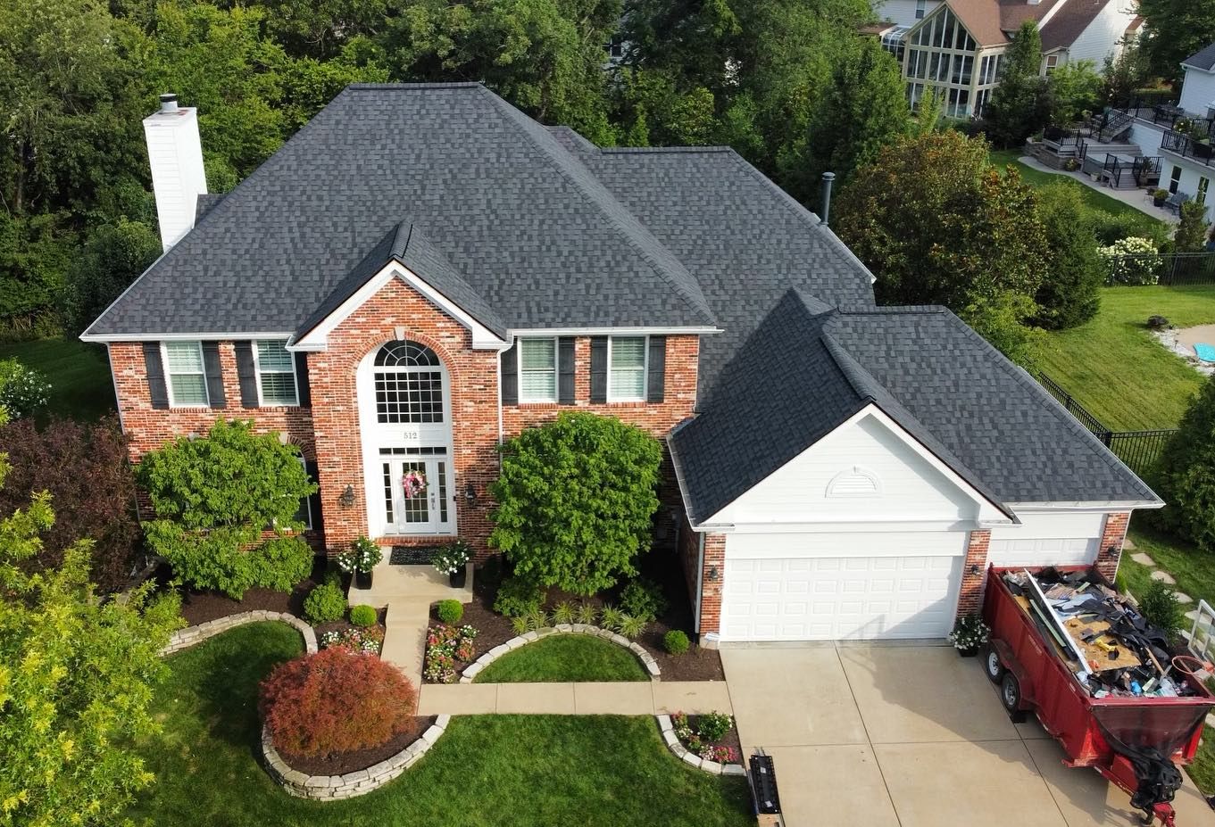 House with new dark gray roof and red brick facade. Dumpster in driveway.
