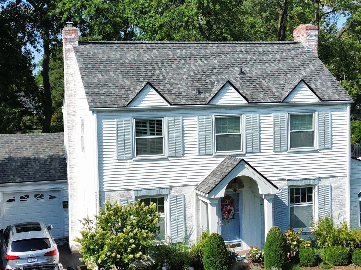 Two-story white house with gray roof, blue shutters, and a car in the driveway.