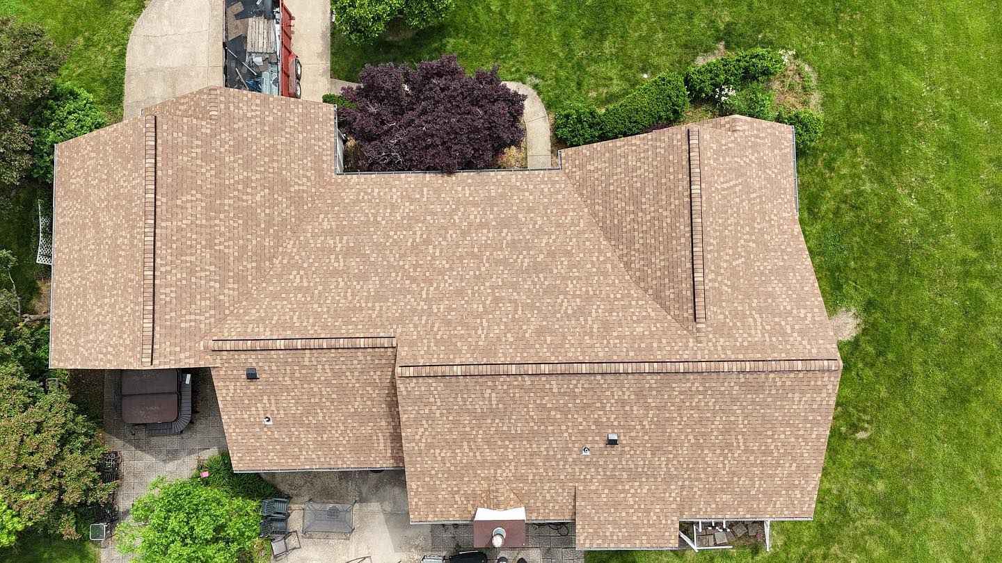 Overhead view of a house with a brown shingled roof, surrounded by green grass and trees.