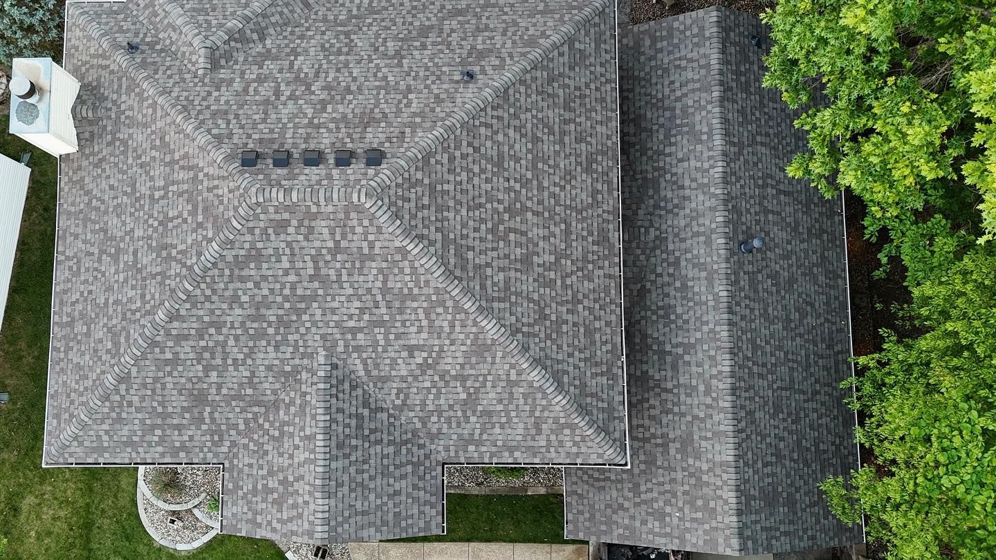 Overhead view of a house with a gray shingled roof, trees, and a small yard.