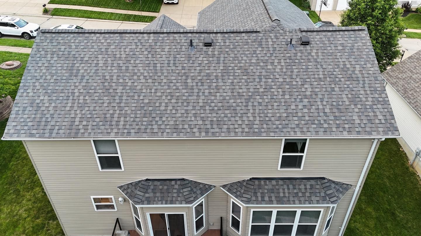 Two-story house with gray shingle roof. Tan siding and grass yard.