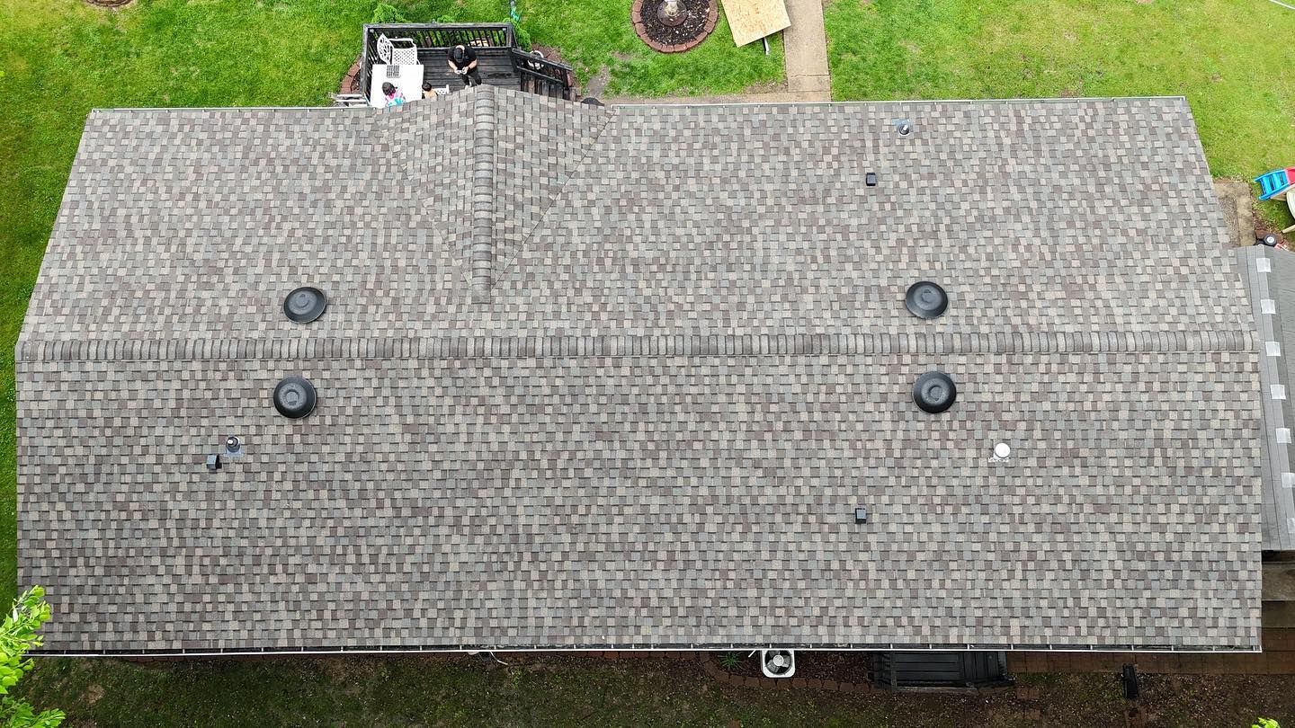 Overhead view of a house roof with four black circular vents. Gray shingles cover the roof.