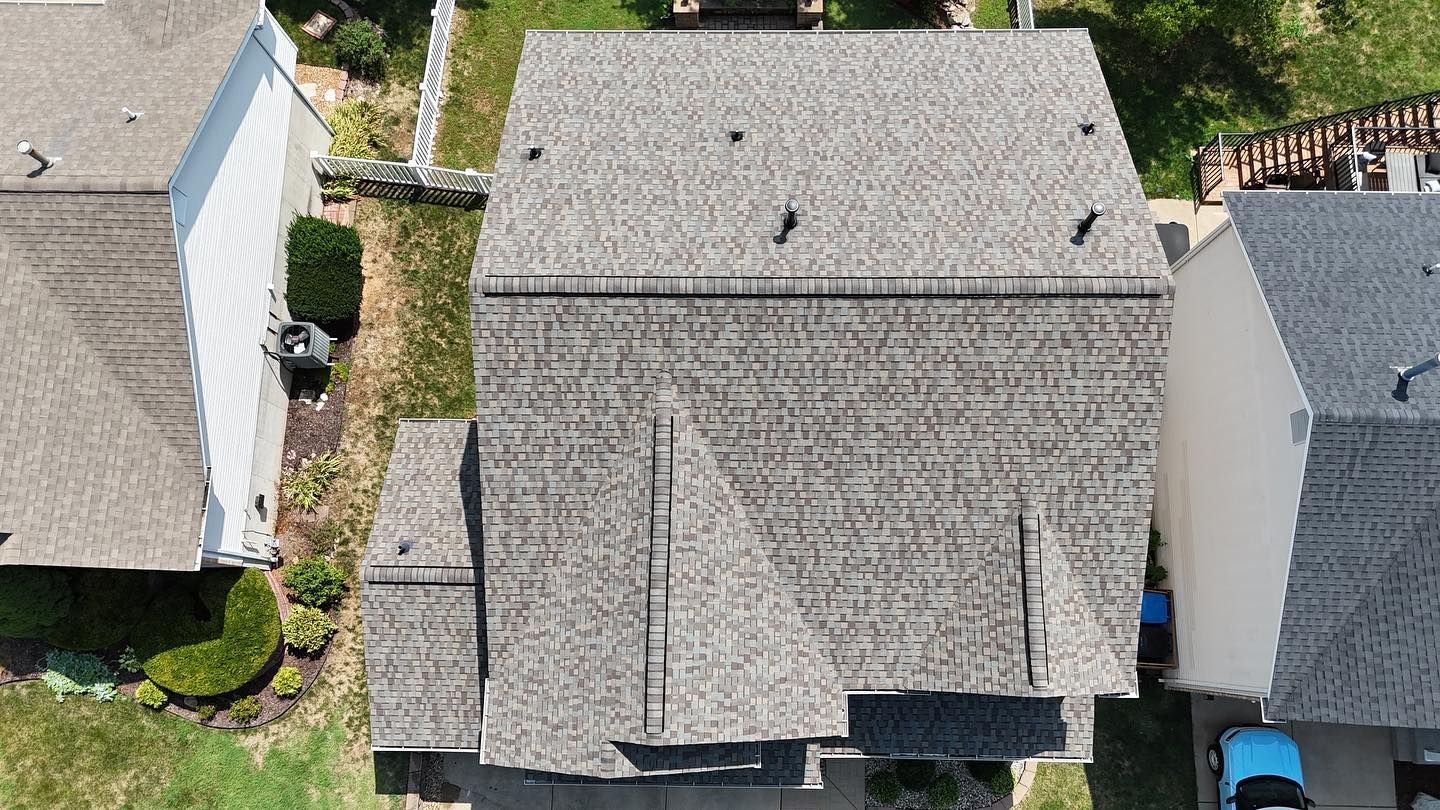 Overhead view of a house with a gray roof, lawn, and surrounding homes.