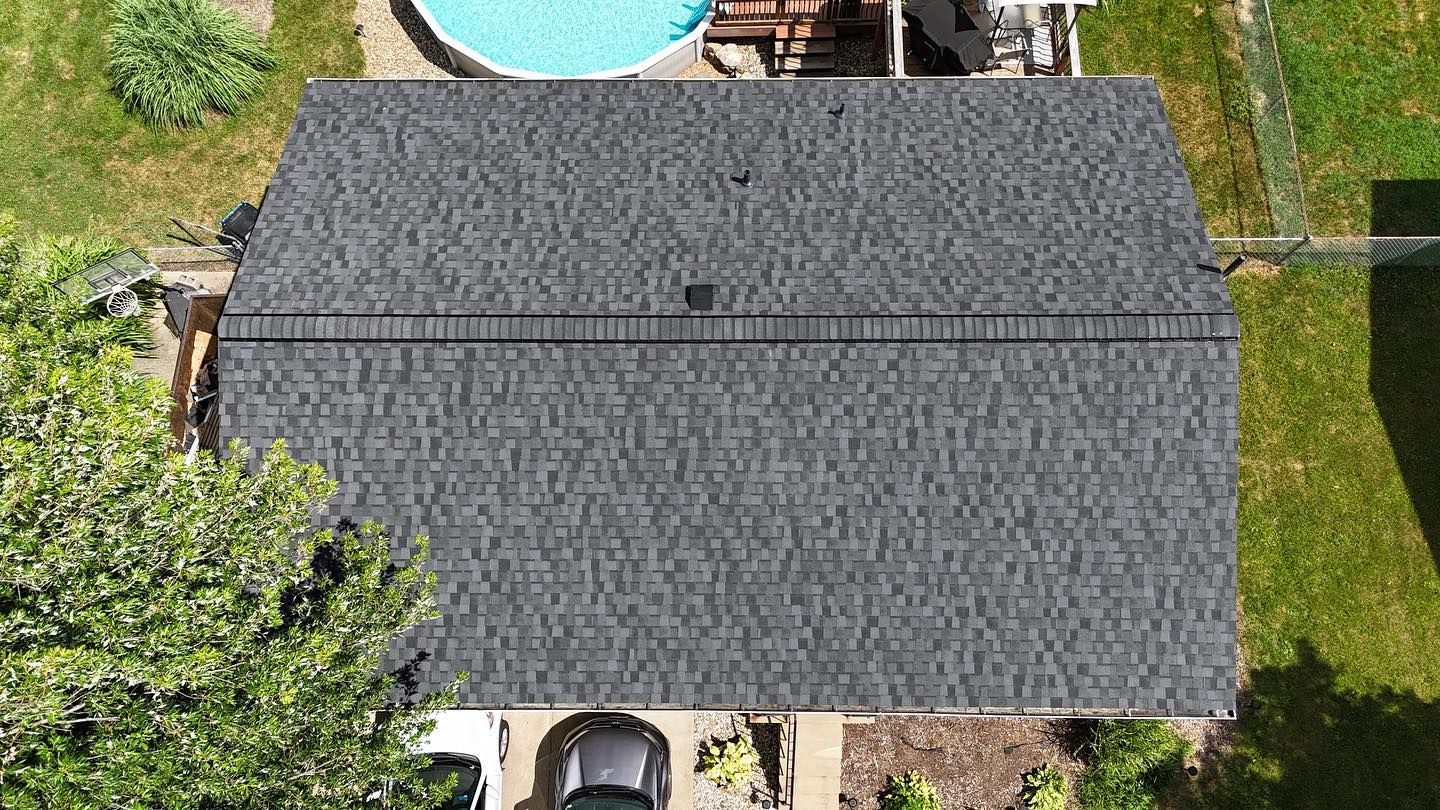 Overhead view of a dark gray shingled roof on a house, with a small black vent and a car parked below.