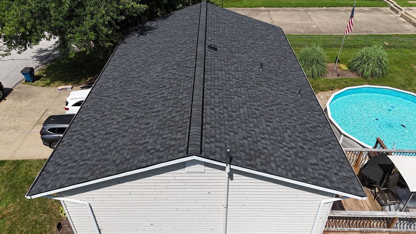 Overhead view of a house with a dark gray shingled roof, a backyard pool, and a flagpole with a US flag.