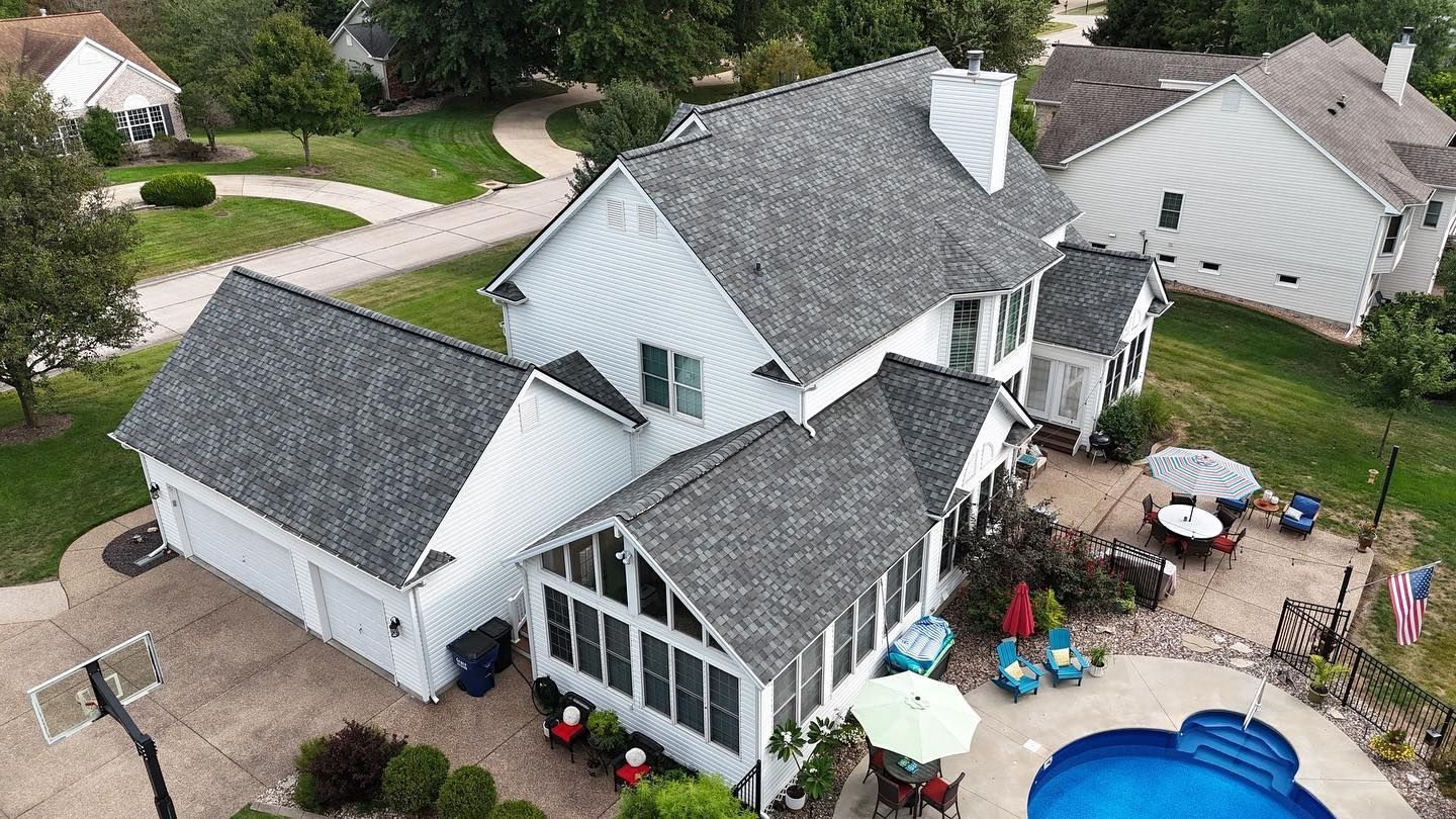 Aerial view of a white house with a gray roof, pool, and patio furniture.