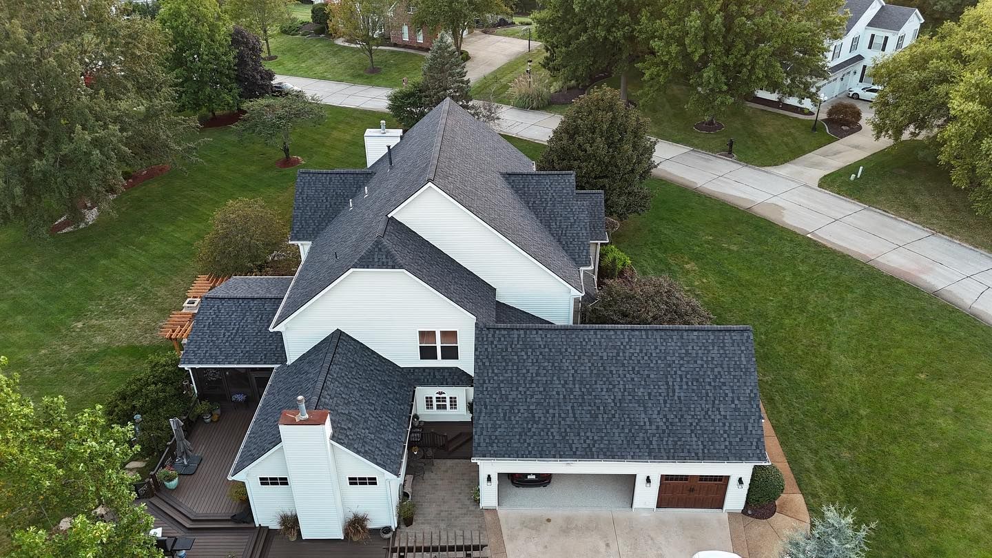 Overhead view of a white two-story house with a gray shingled roof, two-car garage, and landscaped yard.