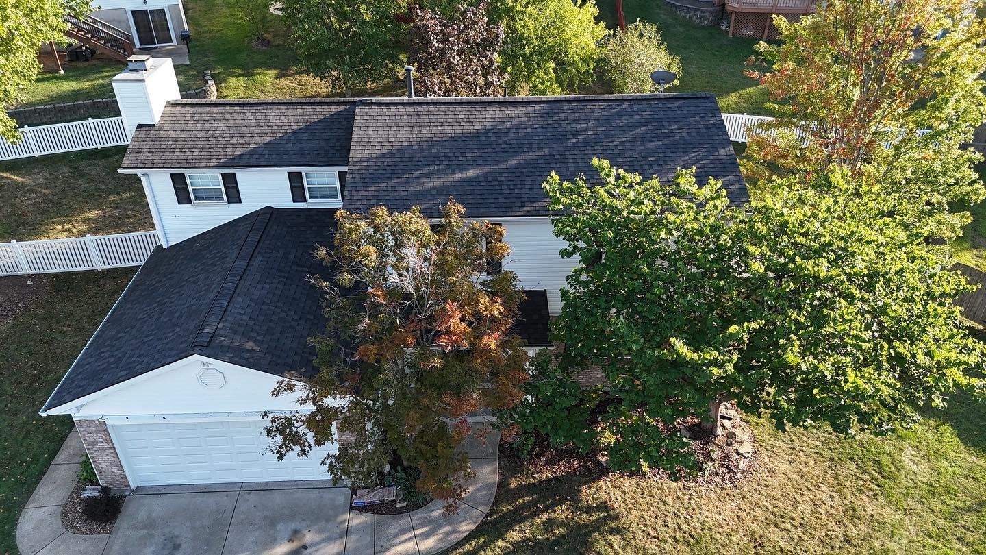 Aerial view of a two-story house with a dark roof and trees in the yard.
