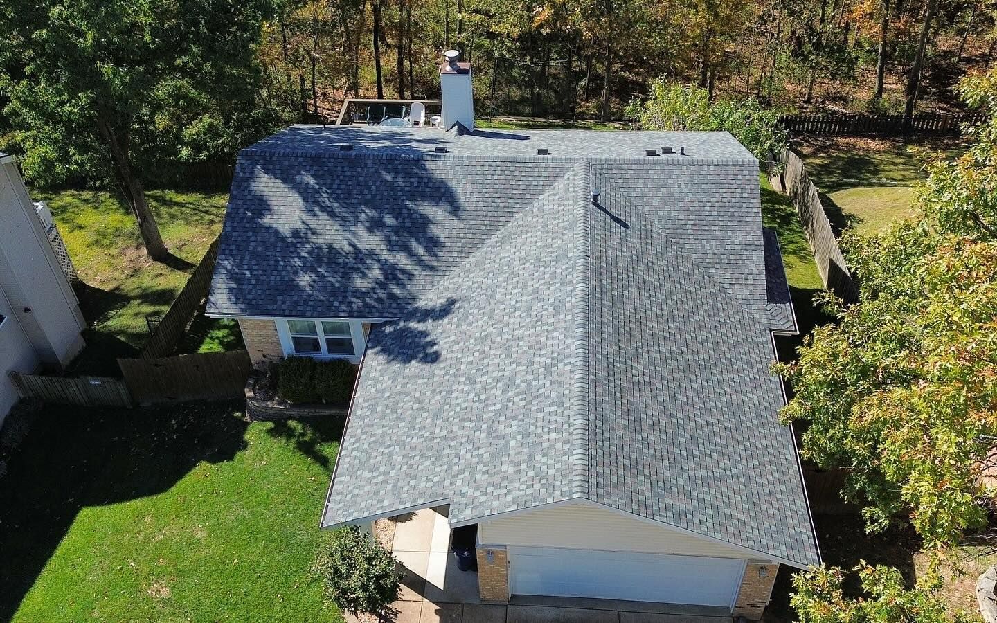 Aerial view of a house with a gray roof, white garage, surrounded by trees and green grass.