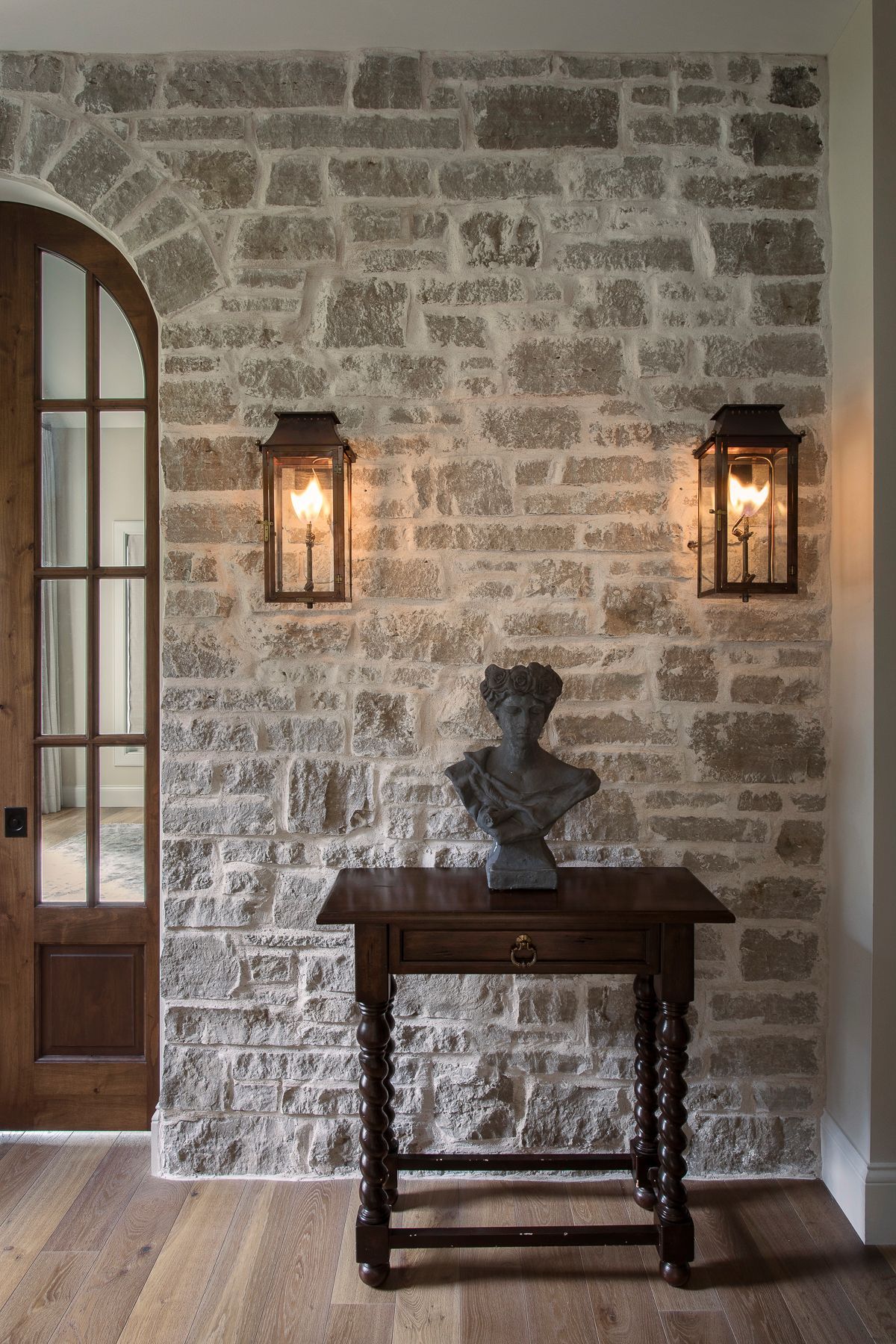 There is a statue of a woman on a table in front of a brick wall.