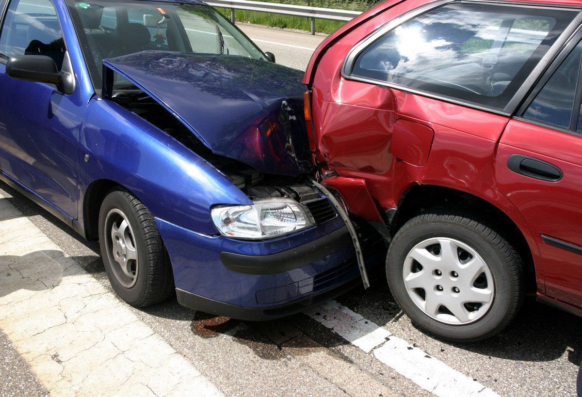 Blue car crashed into a red car on a road, with visible damage to both vehicles.