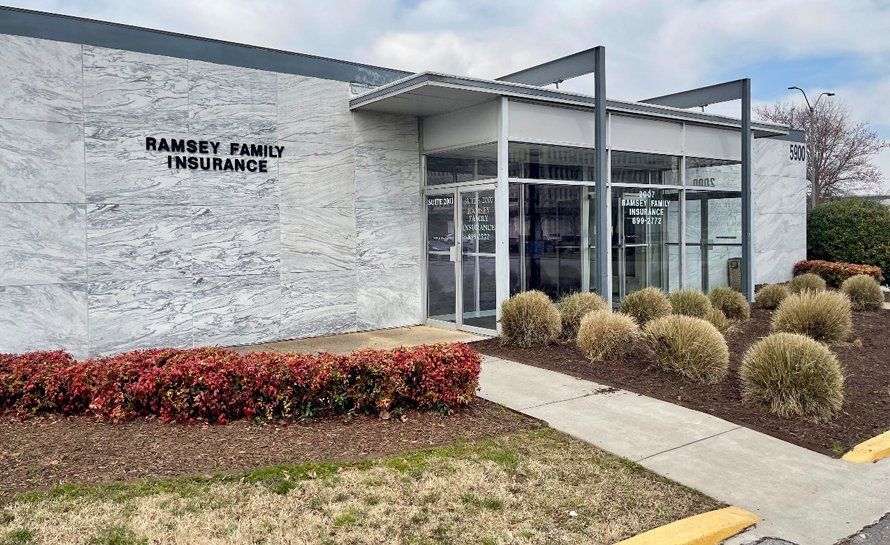 Ramsey Family Insurance building with glass doors, small bushes, and low red hedges.