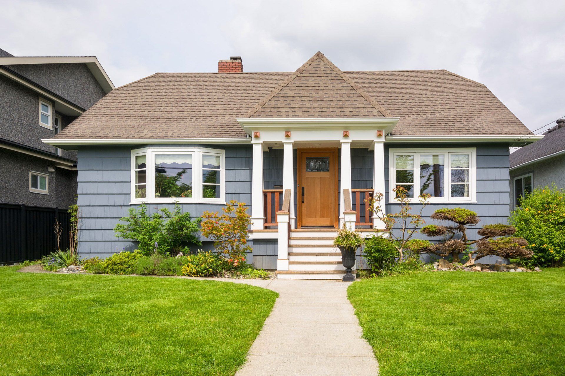 Blue house with brown roof, front porch, and walkway leading to the front door, with green lawn.