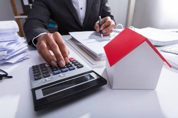 Person calculating finances, near a model house.