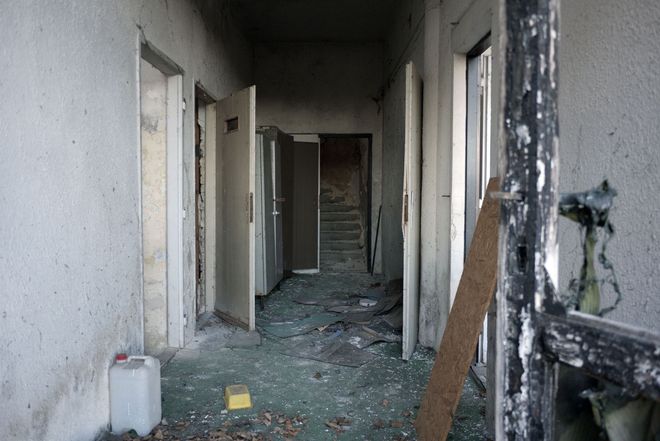 Abandoned hallway with open doors, broken debris on the floor, and peeling walls.