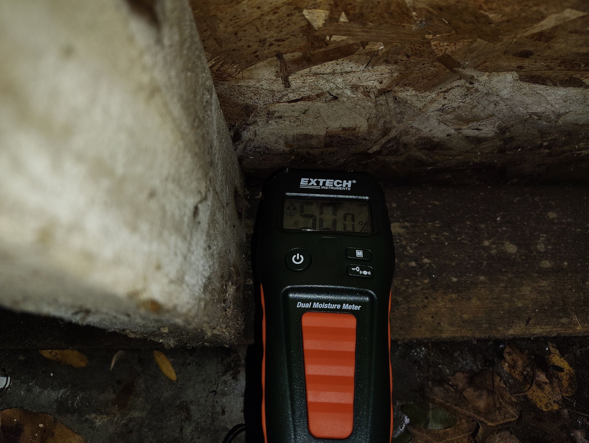 Small black-and-orange device wedged under a stone ledge in a dusty outdoor corner