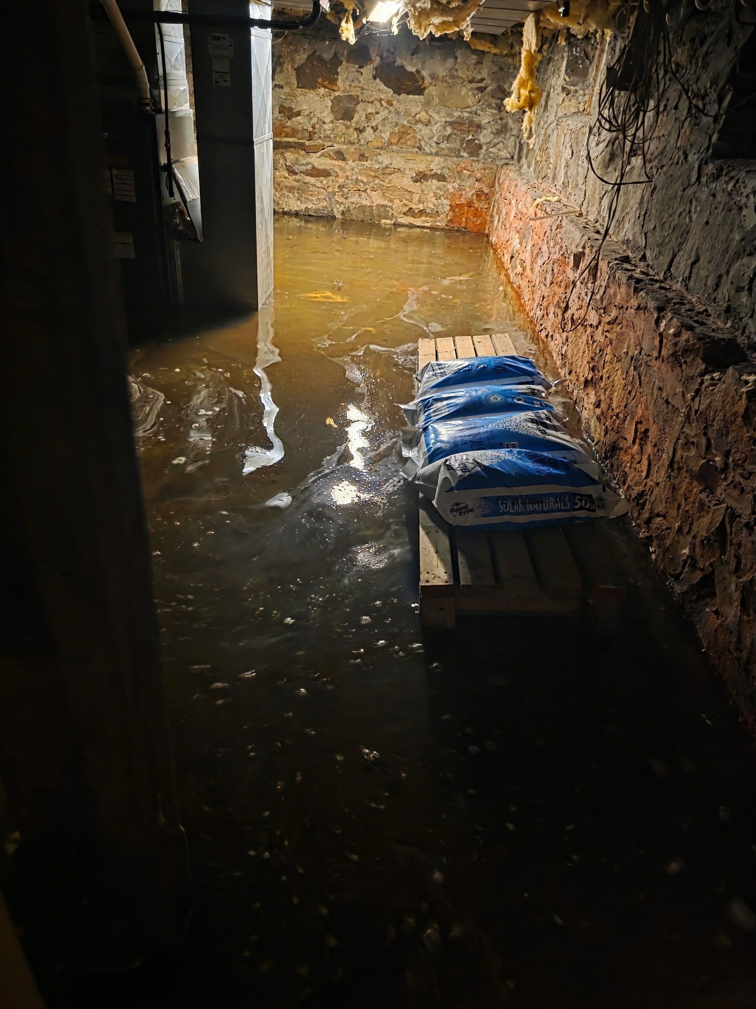 Flooded narrow corridor with muddy water and stacked blue bags on the right.